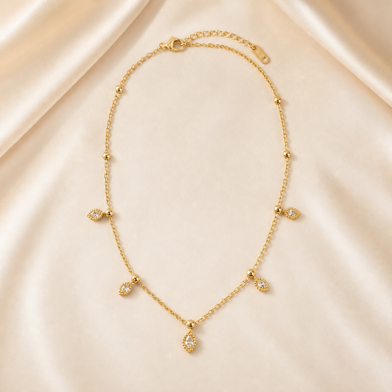 A single gold-toned necklace with a polished yellow-gold finish, built from one fine cable-link chain of small oval links forming a single continuous strand. From the clasp end the chain runs past a series of small polished spherical beads threaded as fixed stations, spaced irregularly: the first two beads occur on plain chain sections, then further beads appear at the points where charms hang.