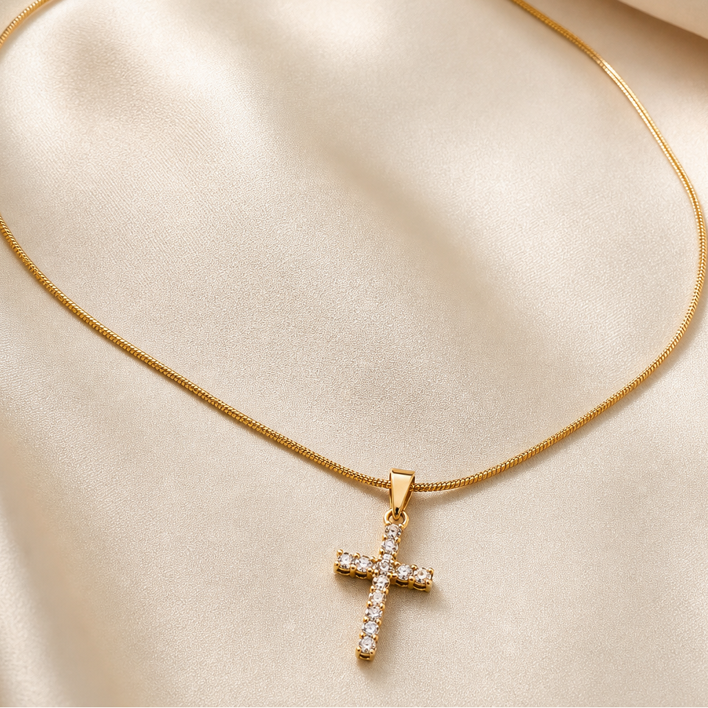A single pendant necklace in yellow-gold-toned metal with a polished finish. It consists of one continuous single-strand snake chain of fine, tight gauge with a smooth, round cross-section, terminating in a small tapered solid-metal bail from which a single cross pendant hangs via a jump ring.