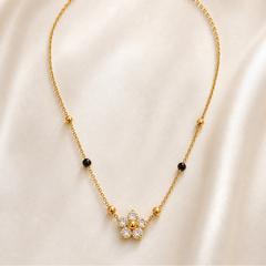 A single gold-tone stainless steel necklace with a polished finish, built on one fine-gauge cable chain strand. From the clasp end: a lobster clasp with a short oval-link extender chain terminating in a small rectangular bar tag; the plain chain continues to the decorative section, where fixed bead stations appear in sequence on each side — first a small round polished gold bead, then a small round black bead, then another small round gold bead — giving four gold beads and two black beads in total, all
