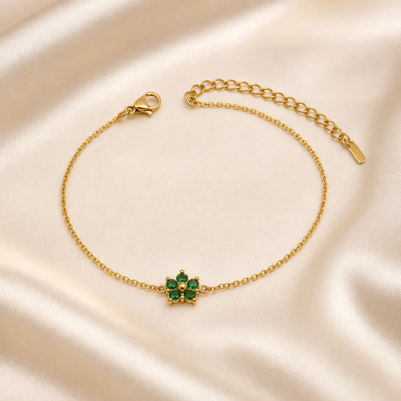 A single flexible bracelet in yellow-gold-toned polished metal, built from one strand of fine oval cable-link chain of light gauge. From the lobster-clasp end, a plain run of chain leads to the single decorative station: a small flower motif set with five round faceted green stones arranged as petals in individual prong/claw settings around a small solid gold-toned domed centre, with tiny gold bead accents between some petals; the flower is fixed inline to the chain via small connector loops and lies flat