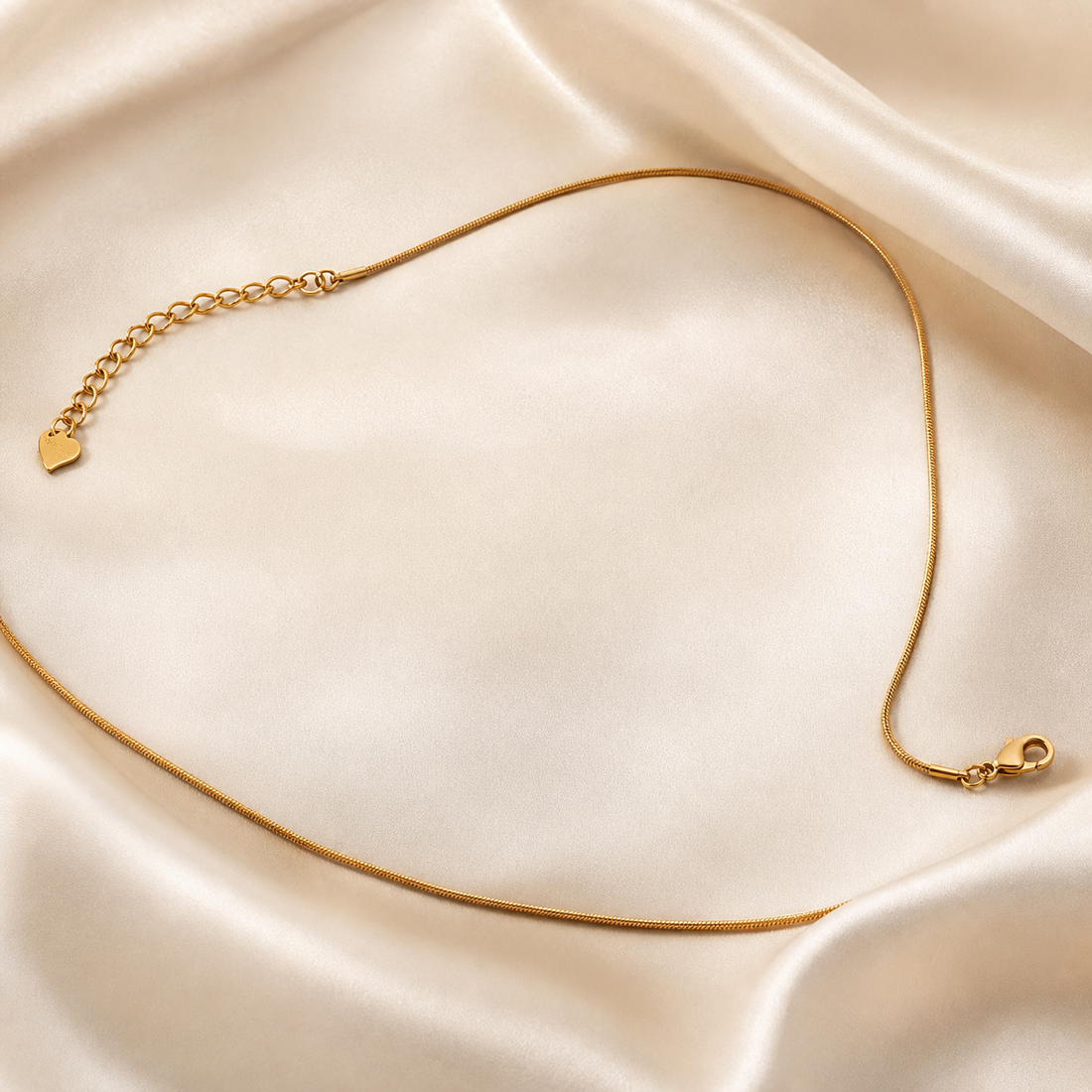 A single gold-tone necklace with a polished finish, constructed as one unbroken strand of very fine, smooth round snake chain of slender gauge. There are no pendants, charms, stations, beads or stones anywhere along the strand; the chain body is entirely plain and uniform.