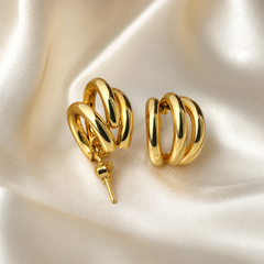 A matched pair of two hoop earrings in yellow-gold-coloured metal with a high-polish, mirror-like finish. Each earring is constructed from two interlocked or concentric smooth rounded tube hoops of slightly different diameters, one nested within the other so they cross and overlap, creating a layered double-hoop silhouette with a domed, channelled relief where the bands cross; the hoops are of medium, even gauge with no stones, pendants, charms or engraving.