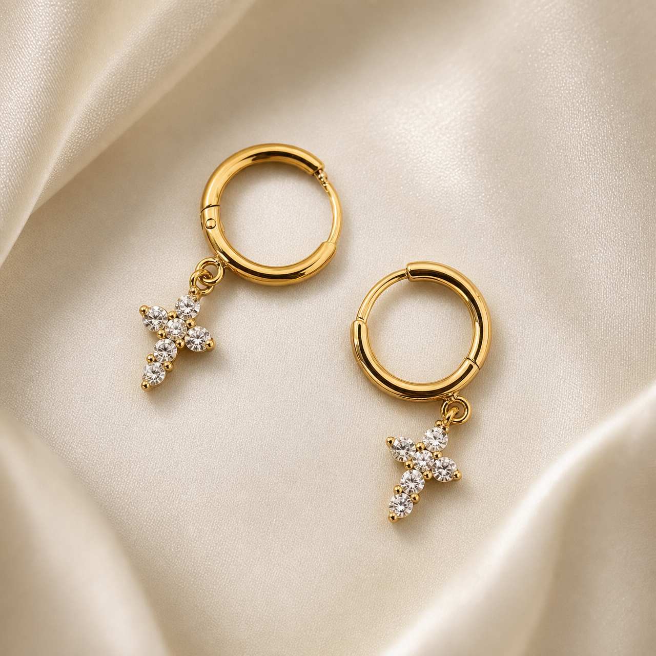 A matched pair of two earrings. Each earring consists of a small hinged huggie hoop in polished yellow gold with a high-shine finish; the hoop is a simple rounded tube of even gauge with a visible hinge seam and a short post closure. Suspended from the base of each hoop by a small jump ring is a dangling cross charm in matching yellow gold, set with six round colourless faceted stones of uniform small size, each held in an individual raised prong-style seat: four stones form the vertical arm and one stone