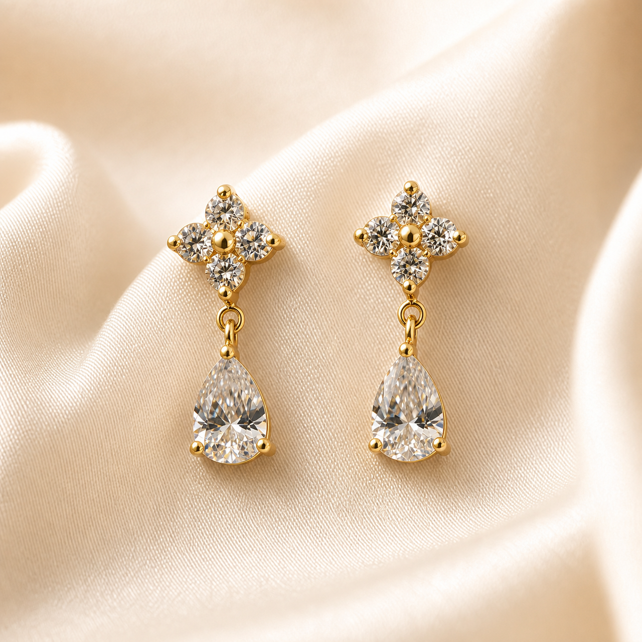 A matched pair of drop earrings, two items total, in a warm gold-coloured polished metal. Each earring comprises a stud top formed as a cross or four-lobed motif and a dangling drop below it. Each stud carries four small round clear faceted stones set as the four arms of the cross, held in small prong or claw settings with gold-coloured bead tips at the outer points, and a single small solid gold-coloured round bead at the centre of the cross.
