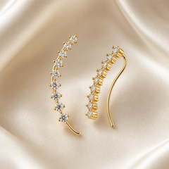 A matched pair of curved ear-climber earrings, two items, in polished yellow-gold-toned metal. Each earring is a single slender arched wire of round gauge, its body set along the outer curve with a graduated row of round, clear, colourless faceted stones in raised multi-prong basket settings; the stones step from smaller at one end to larger mid-row and taper again, with tiny gold prong beads visible between them.