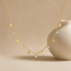 Single-strand station necklace, one piece. Yellow-gold-tone metal with a polished finish; a fine cable chain of small oval links carries dangling stations along its front span, with plain chain continuing to the clasp end, which is partly obscured. The decorated run is roughly thirty times the width of the largest component, a slightly larger clear stone at the centre; any extender is not visible.