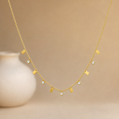 Single gold-tone necklace, one strand of fine polished cable chain with small oval links. Eleven dangling stations are spaced along the front half of the strand, alternating between solid-metal rectangular bar charms and round clear faceted elements; five of the stations are colourless round stones in smooth bezel cups that hang below the chain on short links, and six are flat polished gold-tone rectangles pierced and jump-ring mounted so they swing freely.