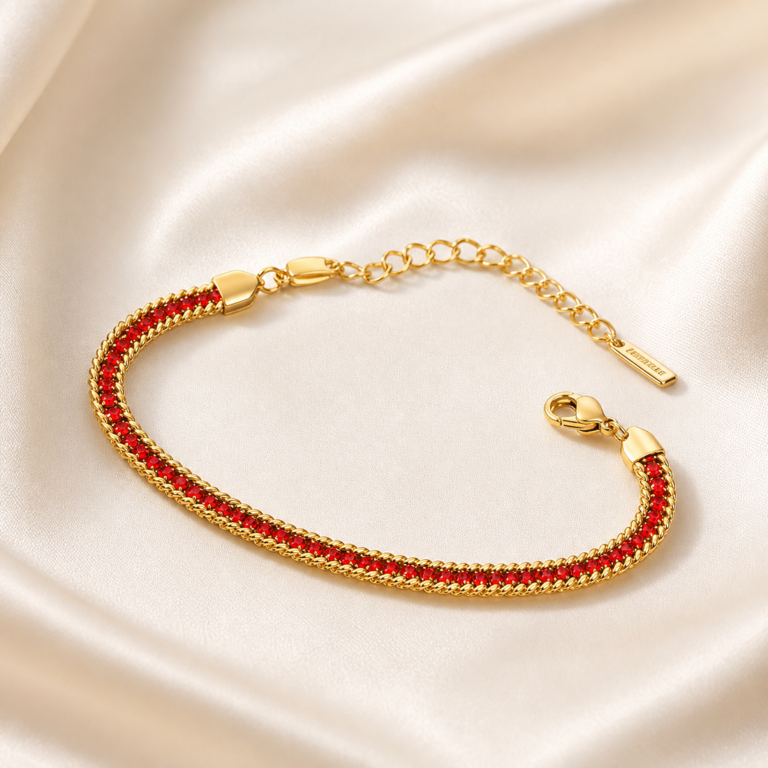 A single flexible bracelet in yellow-gold-toned metal with a polished finish. The main body is a flat, tightly woven herringbone-style chain of fine gauge, bordered on both long edges by a slightly raised twisted rope trim. Set continuously along the centre of the band is one unbroken row of small round faceted red stones, each held in an individual metal bezel or channel setting, the settings matching the gold tone of the chain; the row runs the full decorative length between two smooth, shield-shaped