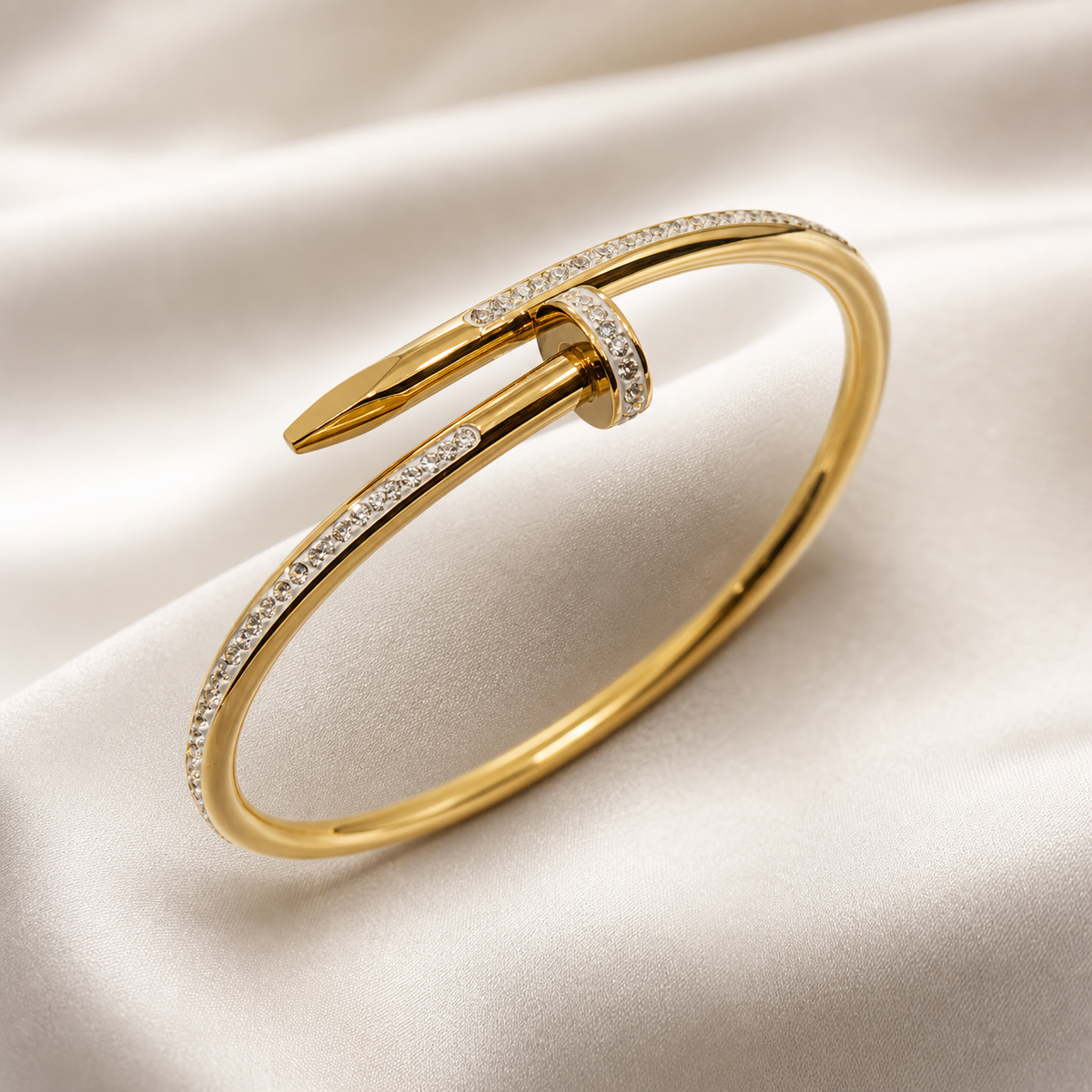 One rigid bangle bracelet formed as a bent nail: a single continuous round-section band of yellow-gold-toned metal with a high-polish finish curves into an open cuff, one end terminating in a flat pointed nail tip, the other end in a larger flat circular nail head that overlaps the shaft.