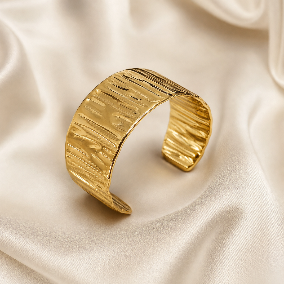 A single rigid cuff bracelet of yellow-gold-toned metal with a high-polish, mirror-like finish. The band is a continuous open cuff of uniform width, solid in construction, with no chain, clasp, hinges or gemstones. Its outer surface carries an all-over hand-hammered or crimped texture of irregular shallow horizontal ridges and dents that run across the width of the band, producing a rippled, bark-like relief; the same ridged texture continues onto the inner wall where visible.