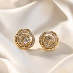 A matched pair of two round stud earrings in yellow-gold-tone polished metal. Each earring is a circular disc built as a low domed cluster: an outer smooth polished gold ring frames an inner crescent band densely set with small round colourless pavé-set stones, while the remaining centre holds an openwork lattice of criss-cross woven gold wire forming a textured nest-like motif, into which a clear faceted element is set.