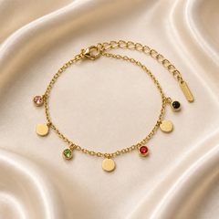 One wrist-worn chain bracelet in yellow-gold-toned metal with a polished finish. It is a single flexible strand of fine cable chain, with one working lobster clasp and a separate extender run of larger oval curb links terminating in one rectangular stamped metal tag; no terminal tag beyond that. The main chain run is approximately thirteen times the width of the largest disc component, and the extender is roughly one third of the main chain length.