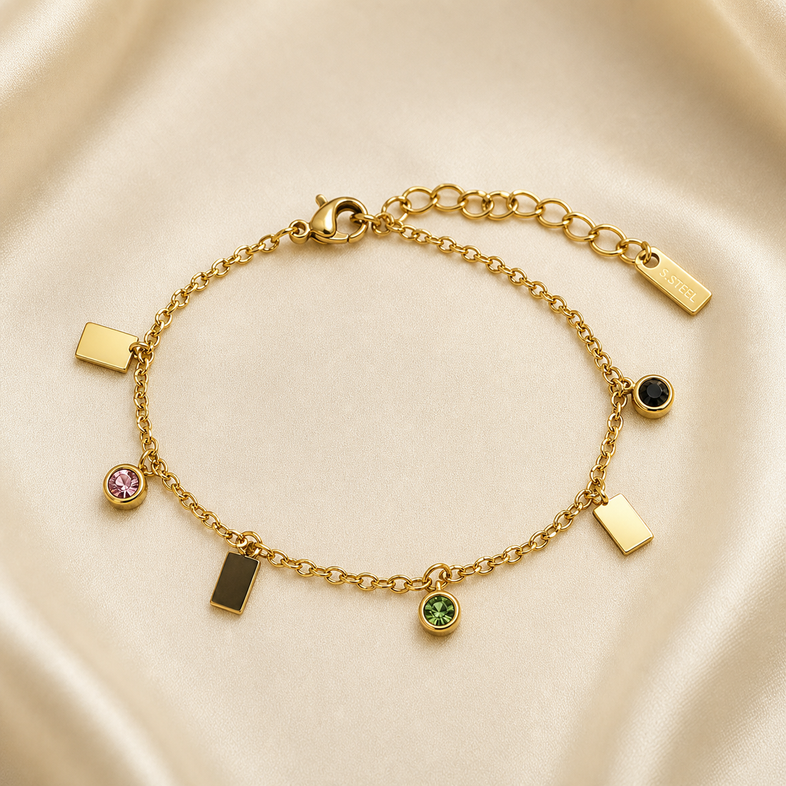 One wrist-worn chain bracelet in yellow-gold-toned metal with a polished finish. It is a single-strand fine cable chain of small oval links, fitted with a working lobster clasp at one end and an extender of larger oval links at the other, terminated by one small rectangular engraved metal tag; the extender is roughly one quarter of the main chain run, and the total chain run is approximately forty times the width of the largest component (a rectangular plate charm).