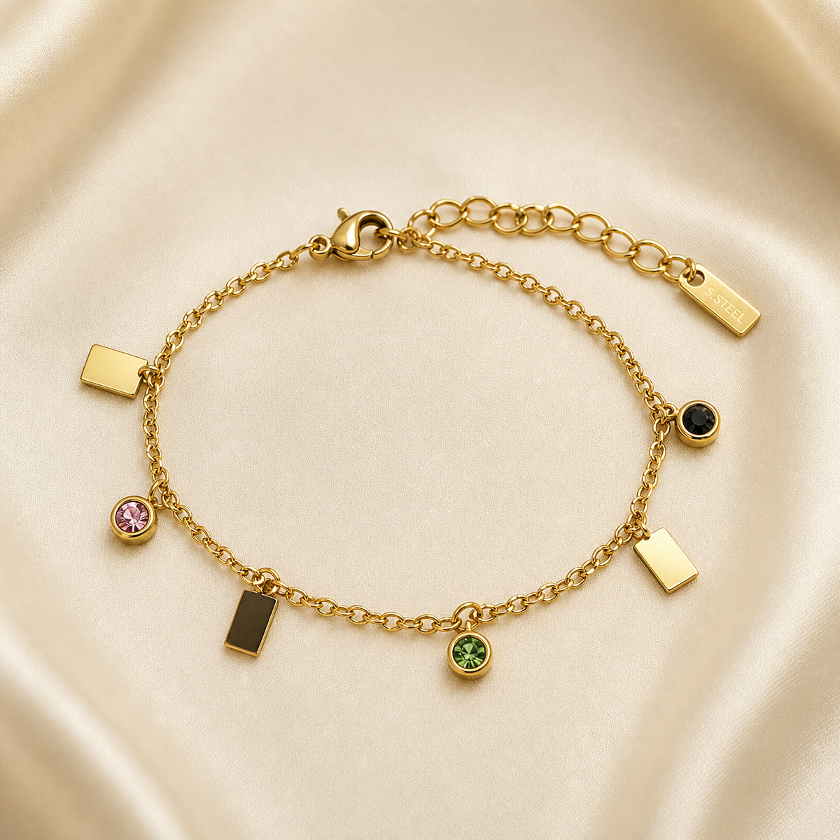 One wrist-worn chain bracelet in yellow-gold-toned metal with a polished finish. It is a single-strand fine cable chain of small oval links, fitted with a working lobster clasp at one end and an extender of larger oval links at the other, terminated by one small rectangular engraved metal tag; the extender is roughly one quarter of the main chain run, and the total chain run is approximately forty times the width of the largest component (a rectangular plate charm).