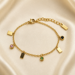 One wrist-worn chain bracelet in yellow-gold-toned metal with a polished finish. It is a single-strand fine cable chain of small oval links, fitted with a working lobster clasp at one end and an extender of larger oval links at the other, terminated by one small rectangular engraved metal tag; the extender is roughly one quarter of the main chain run, and the total chain run is approximately forty times the width of the largest component (a rectangular plate charm).