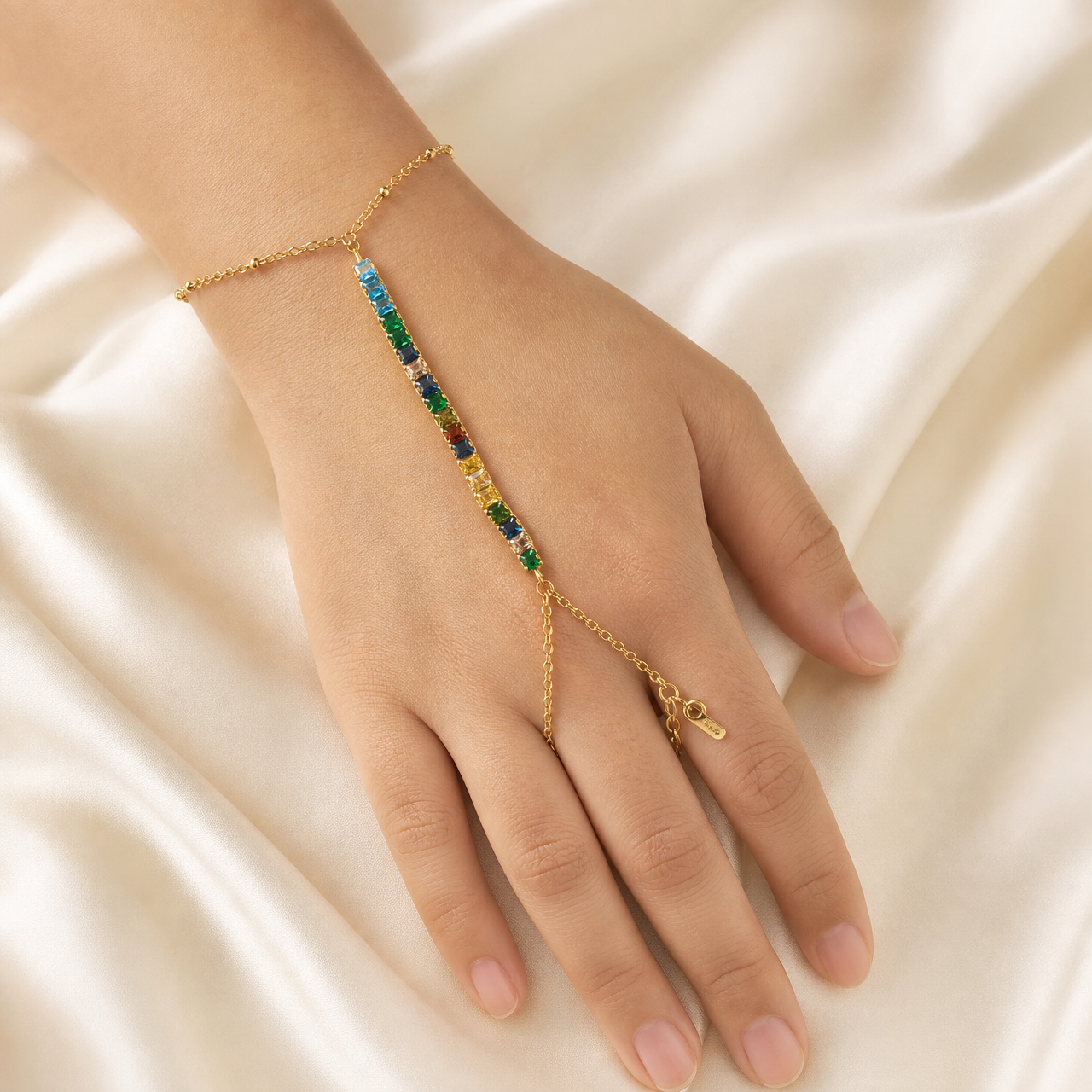 One hand-chain (slave bracelet) in yellow-gold-tone metal with a polished finish. Starting from the clasp end: a fine oval-link cable chain wrist section closes with one lobster clasp and one short extender chain terminated by a single small tag; the wrist chain carries tiny evenly spaced bead accents.