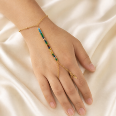 One hand-chain (slave bracelet) in yellow-gold-tone metal with a polished finish. Starting from the clasp end: a fine oval-link cable chain wrist section closes with one lobster clasp and one short extender chain terminated by a single small tag; the wrist chain carries tiny evenly spaced bead accents.