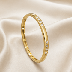One rigid bangle bracelet in yellow-gold-toned metal with a high-polish finish, formed as a continuous closed oval band of medium gauge with a slightly rounded outer profile and flat inner face. One arc of the band carries the decorative work: two short recessed panels set with round clear faceted stones, each panel holding four stones in a straight line, the two groups separated by a plain polished gold segment of roughly the same length; the stones sit in individual channel or bezel-style seats flush