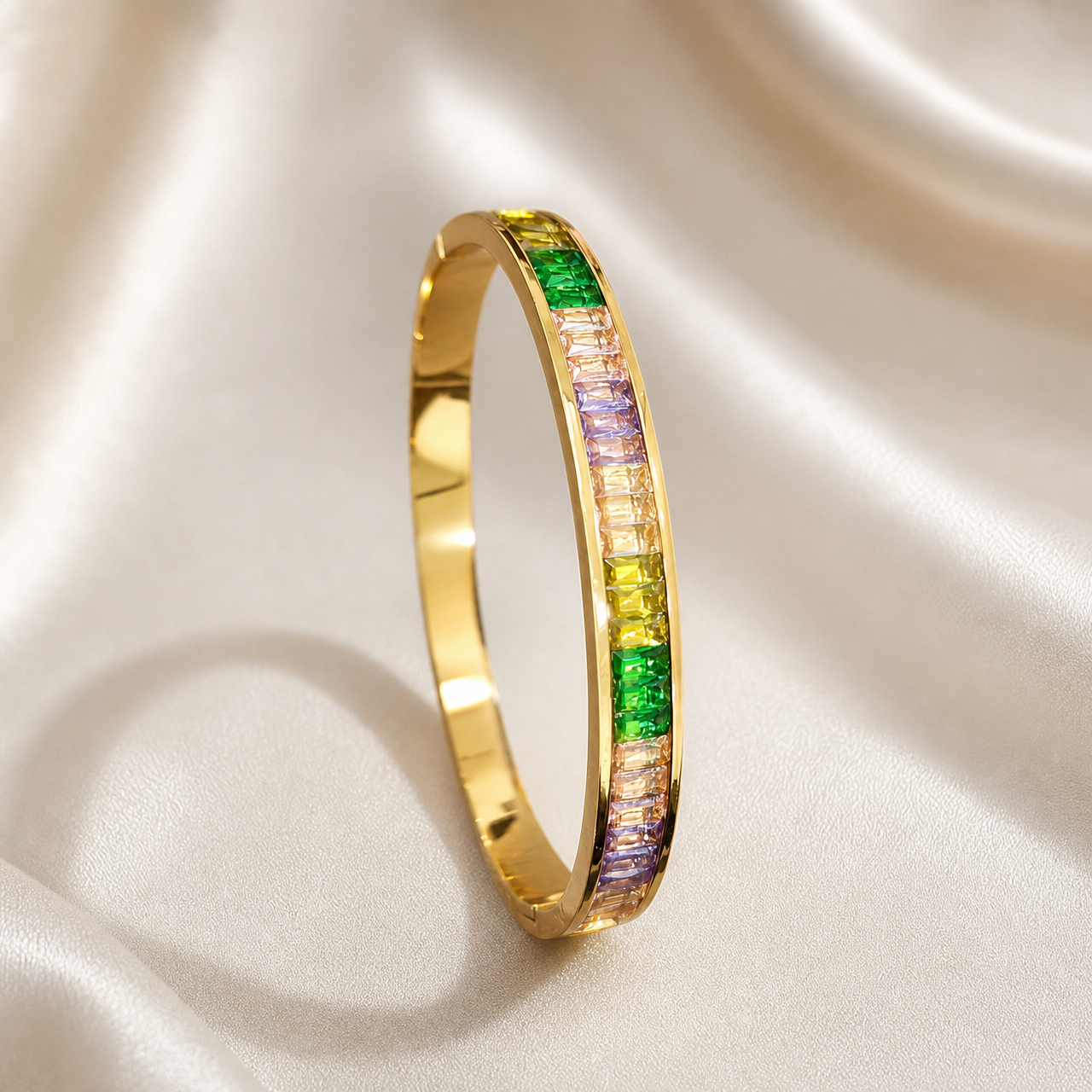 A single rigid oval bangle of polished yellow gold, narrow and uniform in width with a smooth plain inner surface. The outer face carries a continuous channel of baguette-cut coloured stones set edge to edge in a gold channel setting between two raised metal rails, running partway around the band, with one portion of the band left as plain polished gold.