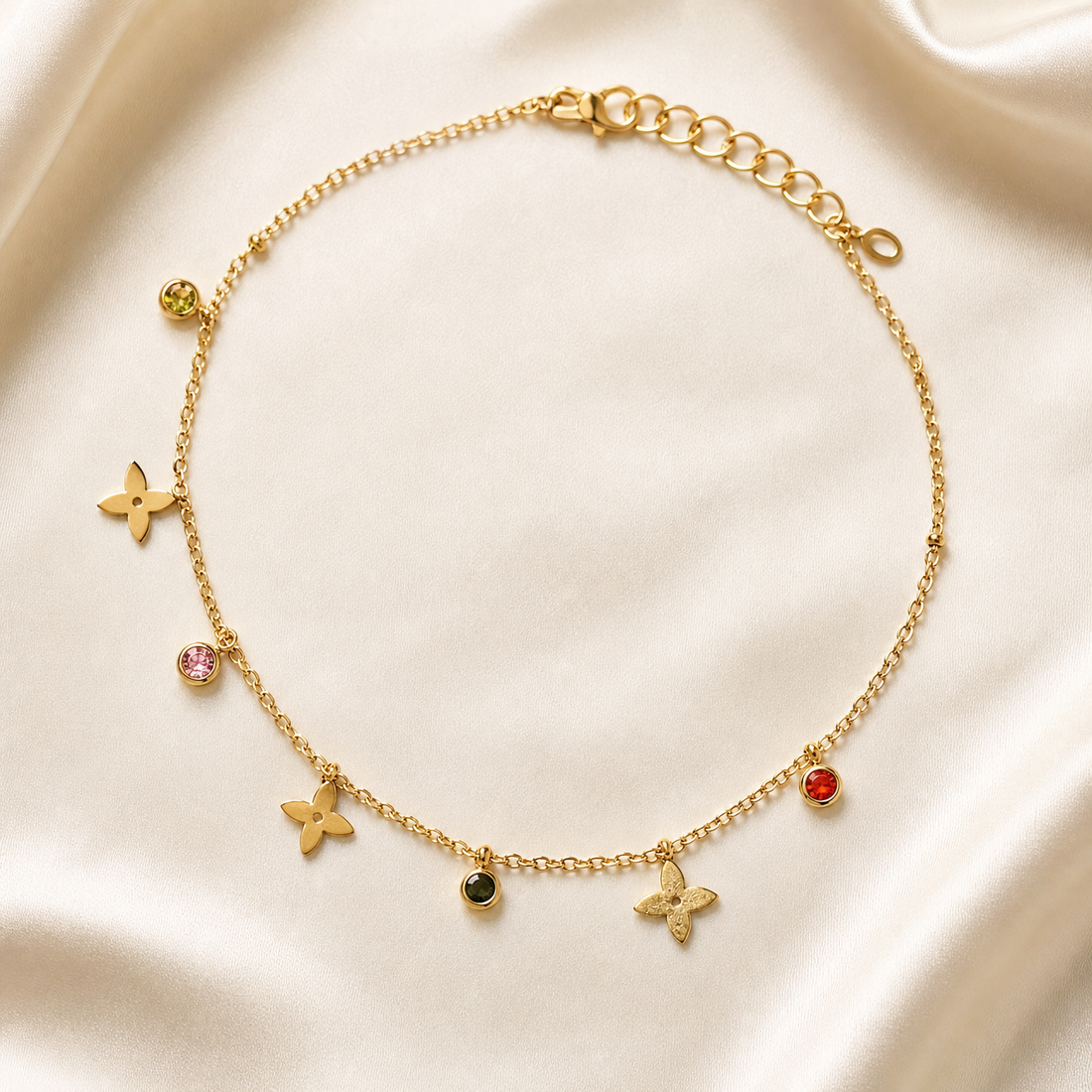 One anklet in gold-tone metal with a bright polished finish. Single-strand fine cable chain of small oval links; the opposite end carries an extender of larger flat oval links roughly one quarter the main chain's length, terminating in a small pierced oval tag, with a working lobster-claw clasp at the other end. The chain run is approximately twenty-five to thirty times the width of the largest charm.