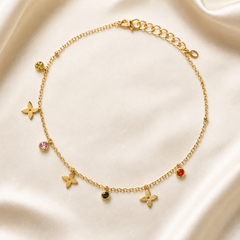 One anklet in gold-tone metal with a bright polished finish. Single-strand fine cable chain of small oval links; the opposite end carries an extender of larger flat oval links roughly one quarter the main chain's length, terminating in a small pierced oval tag, with a working lobster-claw clasp at the other end. The chain run is approximately twenty-five to thirty times the width of the largest charm.