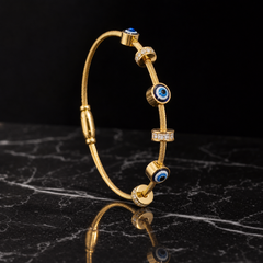 One rigid round bangle in yellow gold with a polished finish. The band is a twisted cable-rope cross-section, even in width all round, roughly one-fifteenth of the outer diameter. It is a fully closed circle with a fixed barrel-shaped fitting on one side. Threaded on the band as sliding charms, ordered around from that barrel: a plain domed gold disc, a small faceted dark-blue stone in a bezel, a gold rondelle channel-set with small white stones, a cylindrical gold bead, a blue-white-black evil-eye disc in