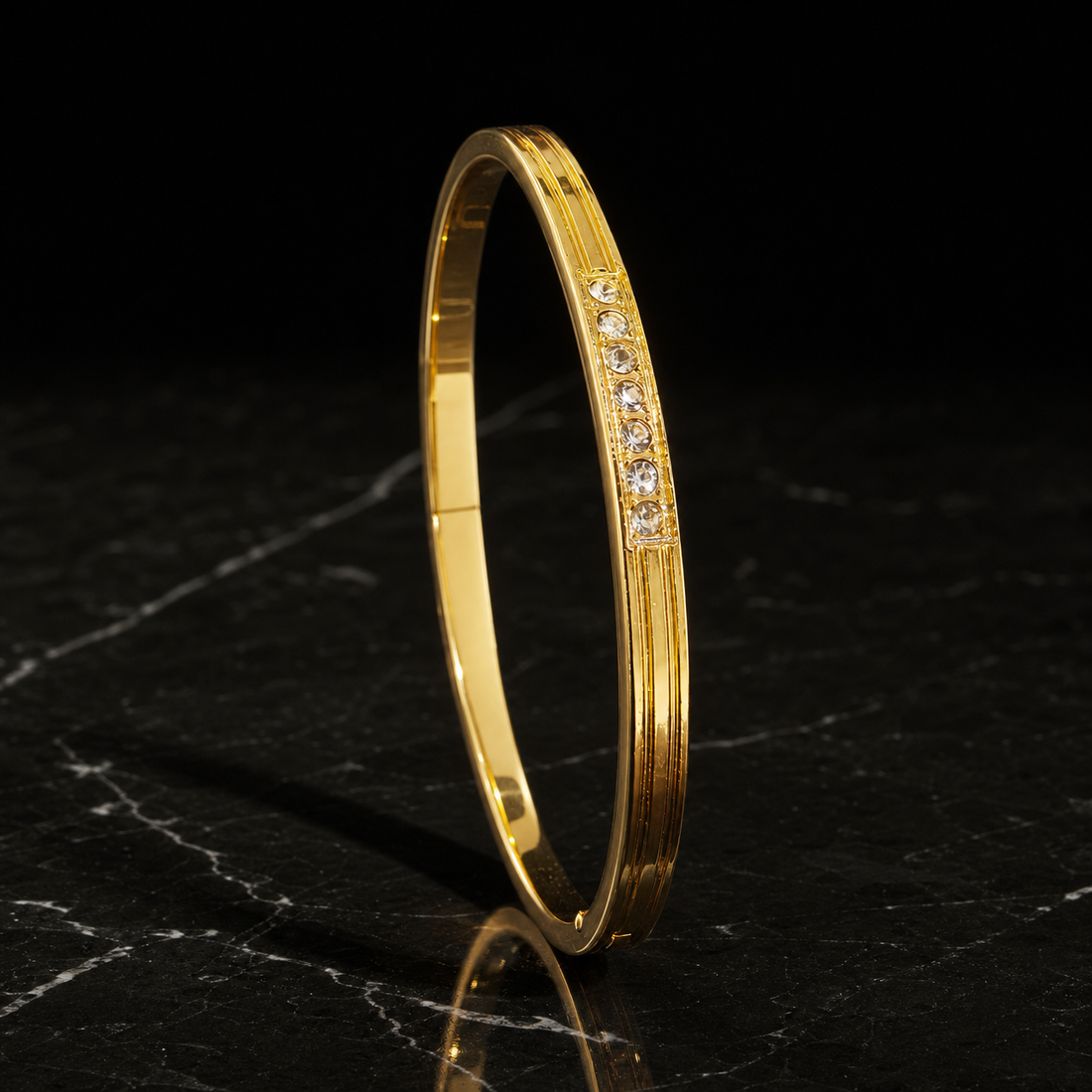 A single rigid bangle in yellow gold with a polished finish. The band is narrow, roughly one-twentieth of the outer diameter in width with a slim thickness, of rounded-to-flat cross-section, even in width all round. It is a hinged bangle with a push-clasp closure seam on the plain section. Along a short raised central face sits a channel-set row of small clear round-cut stones, graduated slightly with the largest at the middle, running only a fraction of the circumference.