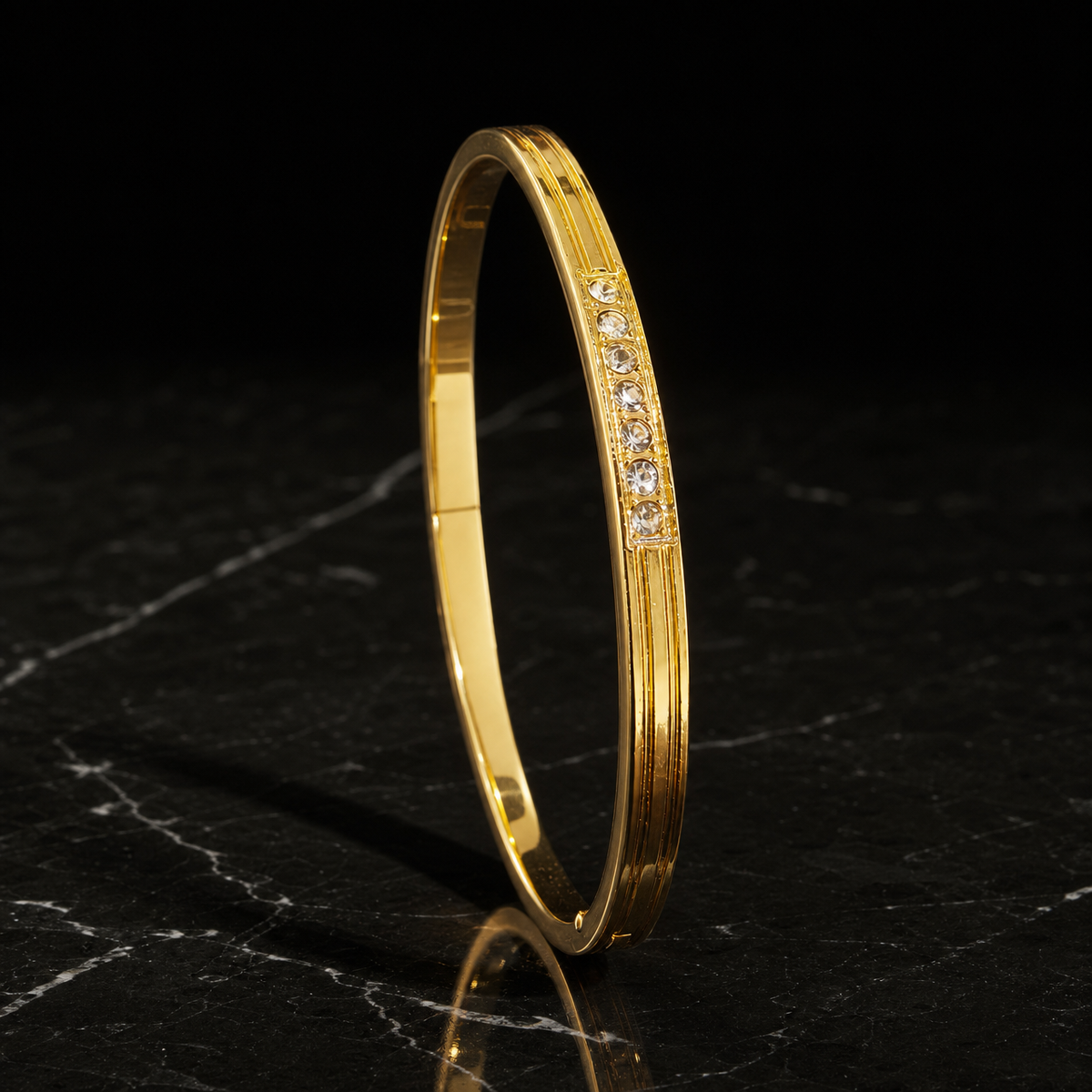A single rigid bangle in yellow gold with a polished finish. The band is narrow, roughly one-twentieth of the outer diameter in width with a slim thickness, of rounded-to-flat cross-section, even in width all round. It is a hinged bangle with a push-clasp closure seam on the plain section. Along a short raised central face sits a channel-set row of small clear round-cut stones, graduated slightly with the largest at the middle, running only a fraction of the circumference.