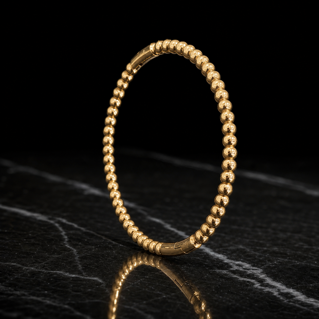 One rigid bangle of yellow-gold-tone metal with a high-polish mirror finish. The band runs about one-tenth of the outer diameter in width, built from a continuous row of identical solid spherical beads, each roughly one-twelfth of the bangle's diameter, forming a rounded beaded cross-section of even width the whole way round with no swelling face. It closes with a hinged opening and an integrated box-clasp segment of smooth plain gold that interrupts the beading.