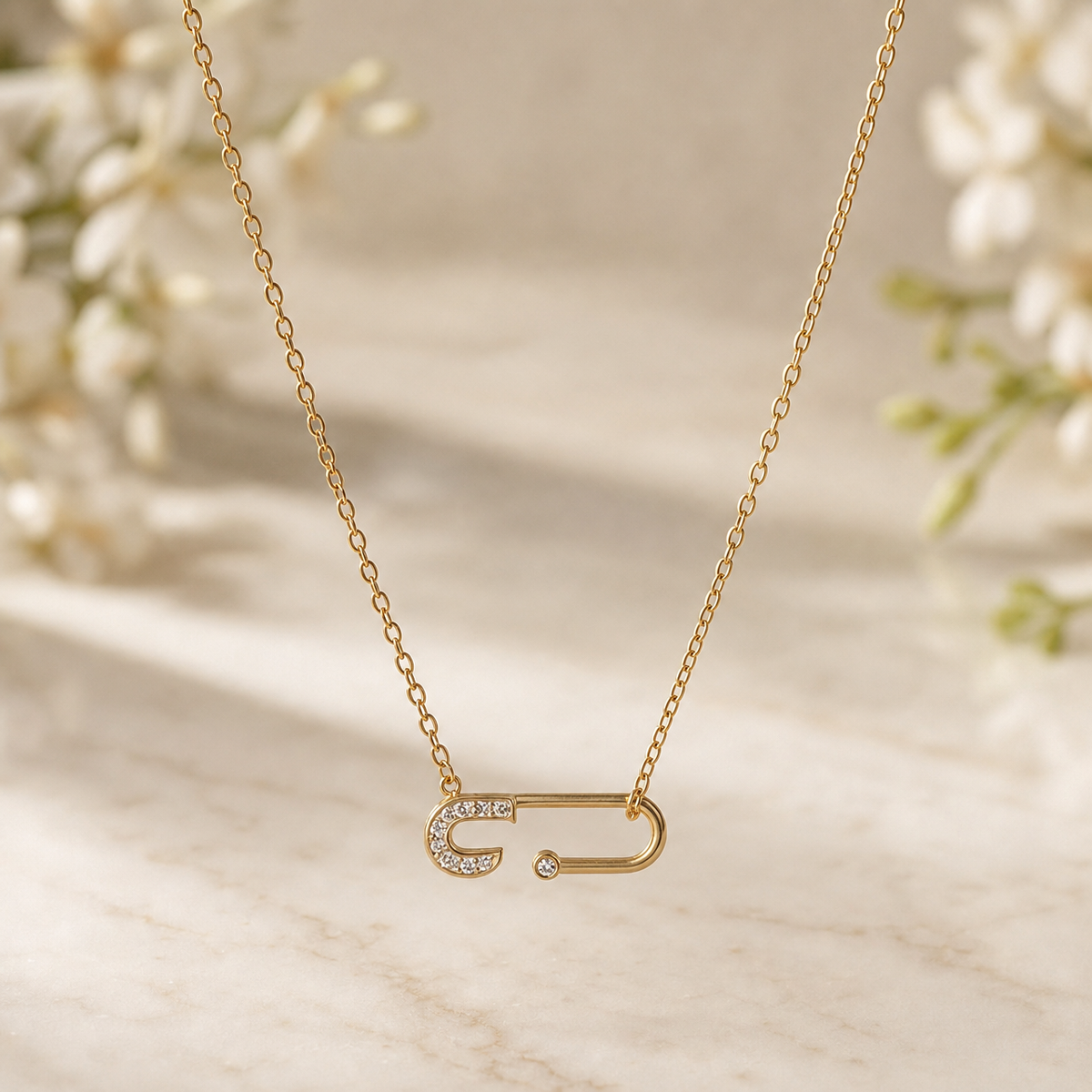 One necklace in yellow-gold-toned metal with a polished finish. A single fine-gauge oval-link cable chain forms one continuous strand, its two ends joined by small jump rings to the ends of a single fixed safety-pin pendant that hangs horizontally as the central feature; the chain run measures roughly 18 times the pendant's width, and no extender is present.