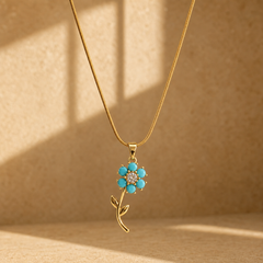One necklace in yellow-gold-toned metal with a polished finish, built as a single fine snake chain of tight, low-gauge links with no branches. The visible chain run is roughly twenty times the pendant's width; no clasp, extender or terminal tag is visible, so the closure is unresolved and likely obscured at the far ends. From the bail end the ledger is: a tapered solid-metal pendant bail, then one dominant flower pendant mounted to the bail by a jump ring.
