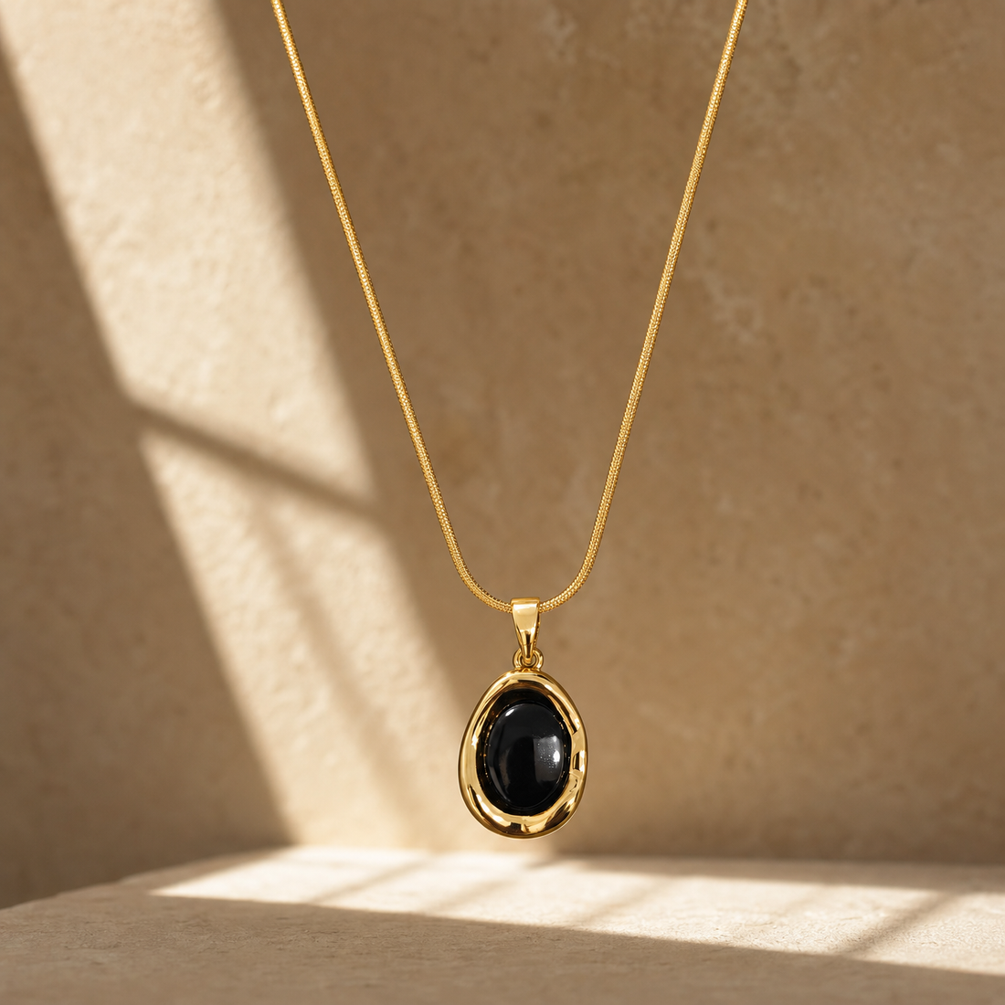 One necklace in yellow-gold-toned metal with a polished finish, built as a single fine-gauge snake chain of round, tightly fitted links, continuous with no branches or stations along its run. The chain run measures roughly 18 to 20 times the width of the pendant, indicating neck length; no extender chain and no working clasp are visible, so the closure is unresolved and partly out of view.