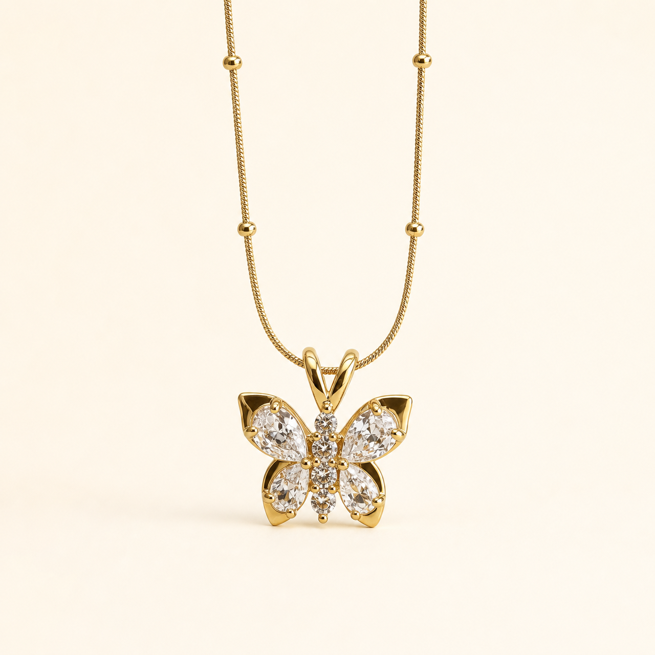 The photograph contains no earrings; the product shown is a single pendant necklace, reported here only because it is the sole visible jewellery piece. It has a yellow-gold polished snake chain fitted with evenly spaced small round metal beads, suspending one solid-metal butterfly pendant.