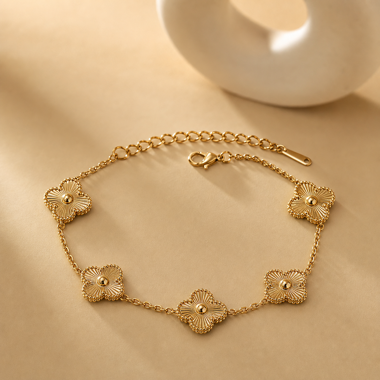 One wrist-worn chain bracelet in yellow-gold-tone metal with a polished finish. It is a single strand of fine, small-gauge cable chain interrupted by five solid-metal quatrefoil (four-lobed clover) stations. From the clasp end: a lobster clasp connects to a short chain run, then the first quatrefoil; chain continues to a second quatrefoil on the opposite side, then a longer chain run to a third, a fourth set close by, and a fifth, with the remaining run terminating in an extender chain of larger oval links