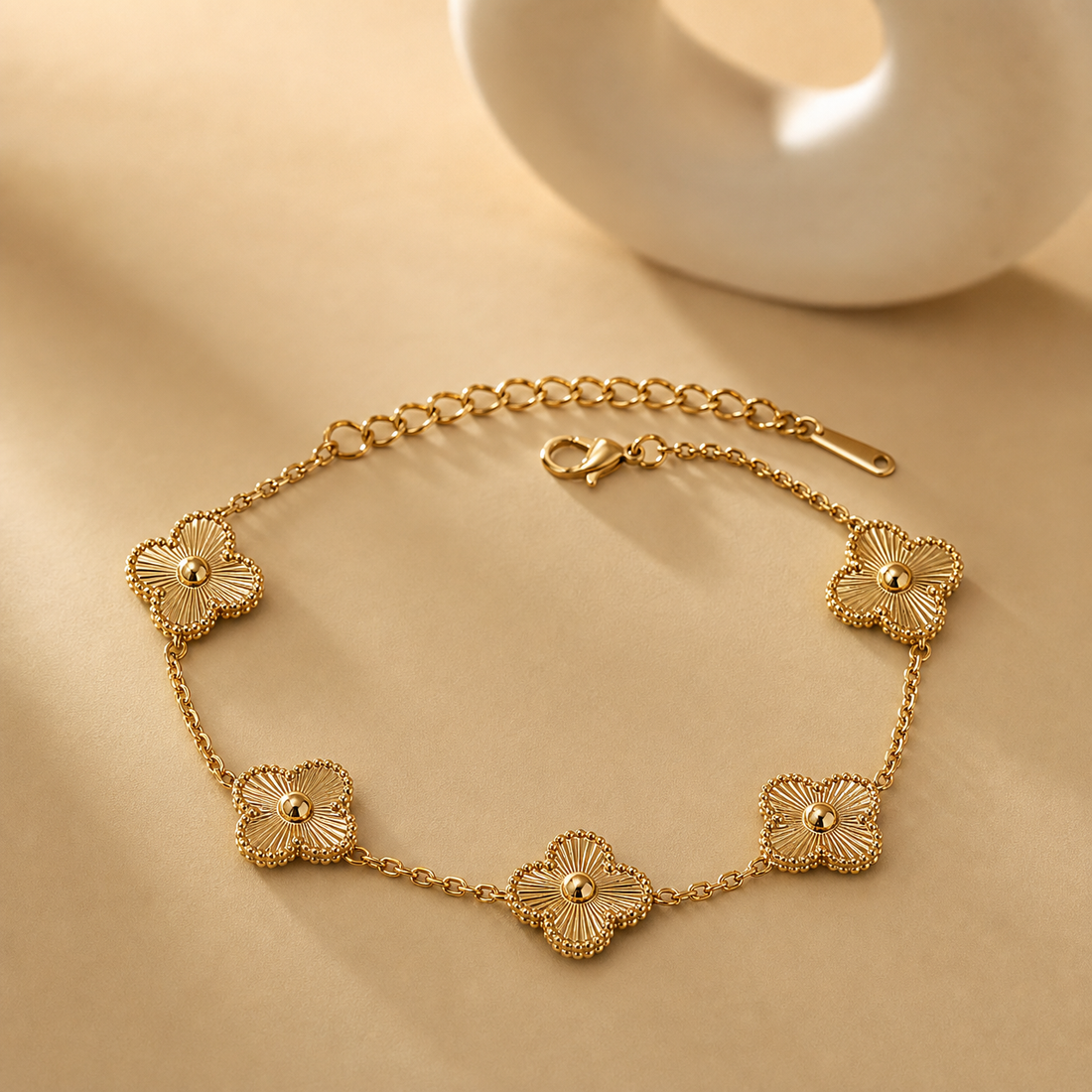 One wrist-worn chain bracelet in yellow-gold-tone metal with a polished finish. It is a single strand of fine, small-gauge cable chain interrupted by five solid-metal quatrefoil (four-lobed clover) stations. From the clasp end: a lobster clasp connects to a short chain run, then the first quatrefoil; chain continues to a second quatrefoil on the opposite side, then a longer chain run to a third, a fourth set close by, and a fifth, with the remaining run terminating in an extender chain of larger oval links