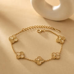 One wrist-worn chain bracelet in yellow-gold-tone metal with a polished finish. It is a single strand of fine, small-gauge cable chain interrupted by five solid-metal quatrefoil (four-lobed clover) stations. From the clasp end: a lobster clasp connects to a short chain run, then the first quatrefoil; chain continues to a second quatrefoil on the opposite side, then a longer chain run to a third, a fourth set close by, and a fifth, with the remaining run terminating in an extender chain of larger oval links