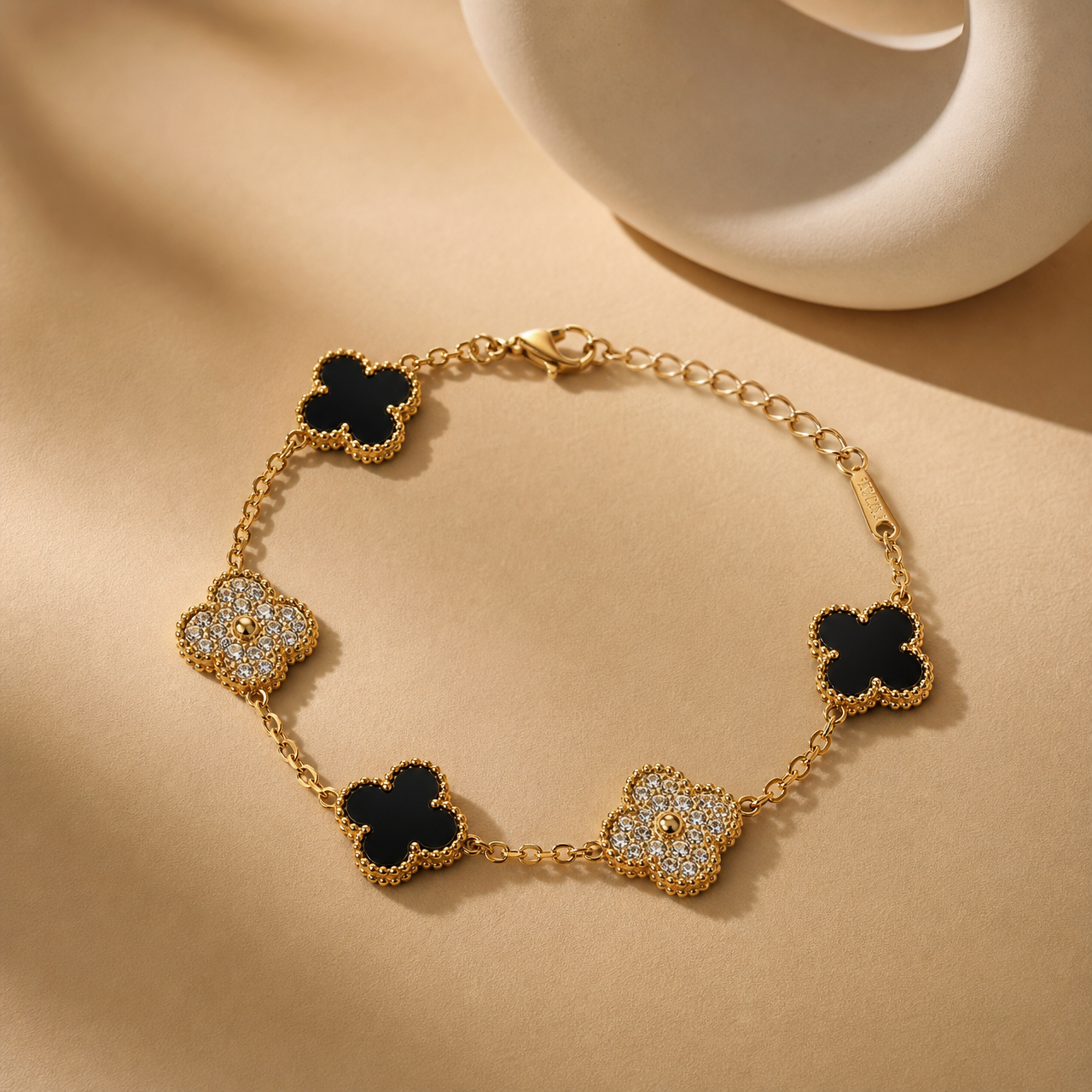 One wrist-worn chain bracelet in yellow-gold-tone metal with a polished finish and beaded-wire edging on its motifs. Construction is a single strand of fine-gauge oval cable chain linking five quatrefoil (four-lobed clover) station motifs, each mounted as a fixed station joined into the chain by small rings. The total chain run is roughly 14 times the width of the largest motif, and the extender section beyond the last motif is about one third of the main chain. A working lobster clasp is visible.