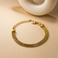 One wrist-worn chain bracelet in warm yellow-gold-tone metal with a polished finish. Construction is a multi-strand bundle of fine, narrow, flattened curb-style chains of small gauge, gathered at each end into solid tapered trapezoidal end caps that bind the strands; the strands hang with slight unevenness between the caps. The chain run between the caps is approximately twelve to fourteen times the width of one end cap. A working lobster-claw clasp is visible, attached by a jump ring to one end cap.