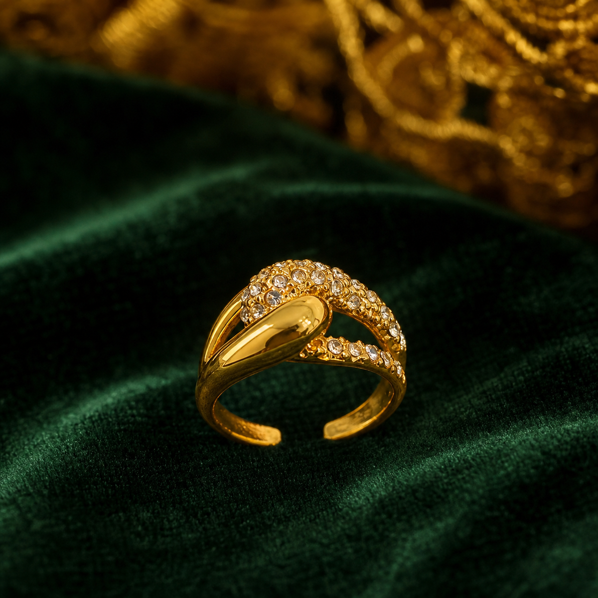 The photograph shows one ring, not earrings: a single gold-tone finger ring with a polished yellow-metal finish. The band splits into two curving arms that cross over one another; one arm is a smooth, polished solid-metal ribbon, while the other carries a continuous pavé field of small round clear faceted elements set into the metal. The band is open-backed with an adjustable gap. Construction is a single rigid piece with no articulation, hinges, drops or dangling components.