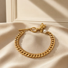 One wrist-worn chain bracelet in warm yellow-gold-toned metal with a polished finish. The construction is a single continuous run of heavy flattened curb links of medium gauge, with a second fine cable chain running parallel alongside the main curb chain for most of its length, effectively a double-strand chain. The main chain run is approximately 15 to 18 times the width of the largest component, the toggle bar; there is no separate extender chain, so the extender fraction is zero.