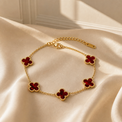 A single wrist-worn chain bracelet in yellow-gold-toned metal with a polished finish. It is a single-strand fine cable chain of small oval links, with no branches. The chain run is approximately 12 times the width of the largest component (one clover motif); the extender chain, made of larger oval links, is roughly one quarter the length of the main chain. A working lobster-claw clasp is visible, plus one extender chain terminating in a single elongated oval metal tag with one drilled hole.