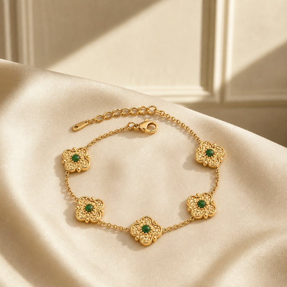 One wrist-worn chain bracelet in yellow-gold-tone metal with a bright polished finish. Construction is a single strand of fine-gauge cable chain interrupted by five matching stations; each station is a solid-metal four-lobed flower or quatrefoil motif with a hammered, textured surface, small bead accents at the lobe tips, and a round, smooth green cabochon-set centre stone in a bezel mounting.