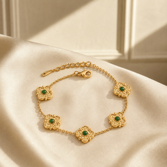 One wrist-worn chain bracelet in yellow-gold-tone metal with a bright polished finish. Construction is a single strand of fine-gauge cable chain interrupted by five matching stations; each station is a solid-metal four-lobed flower or quatrefoil motif with a hammered, textured surface, small bead accents at the lobe tips, and a round, smooth green cabochon-set centre stone in a bezel mounting.