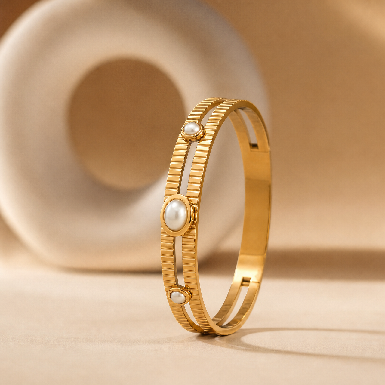 One rigid gold-tone bangle with a polished finish. The band is formed as two slender parallel rails joined into a single hoop, each rail roughly one-eighth of the outer diameter apart, with a flat cross-section and even width all round; both rails carry a continuous cast vertical ribbed or slatted pattern running the full visible circumference. From the face: a central large oval white pearl cabochon in a smooth gold bezel, flanked on each side by a smaller round white pearl in a matching round bezel.