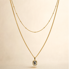A two-strand necklace set in yellow-gold-tone metal with a polished finish. The set comprises two parallel strands joined at shared ends: a shorter, fine snake-style chain carrying small spherical bead stations spaced at irregular intervals along its run, and a longer, fine-gauge curb link chain from which a single pendant hangs. The longest chain run measures roughly 40 times the width of the pendant, the largest component; the shorter strand is approximately three-quarters the length of the long chain.