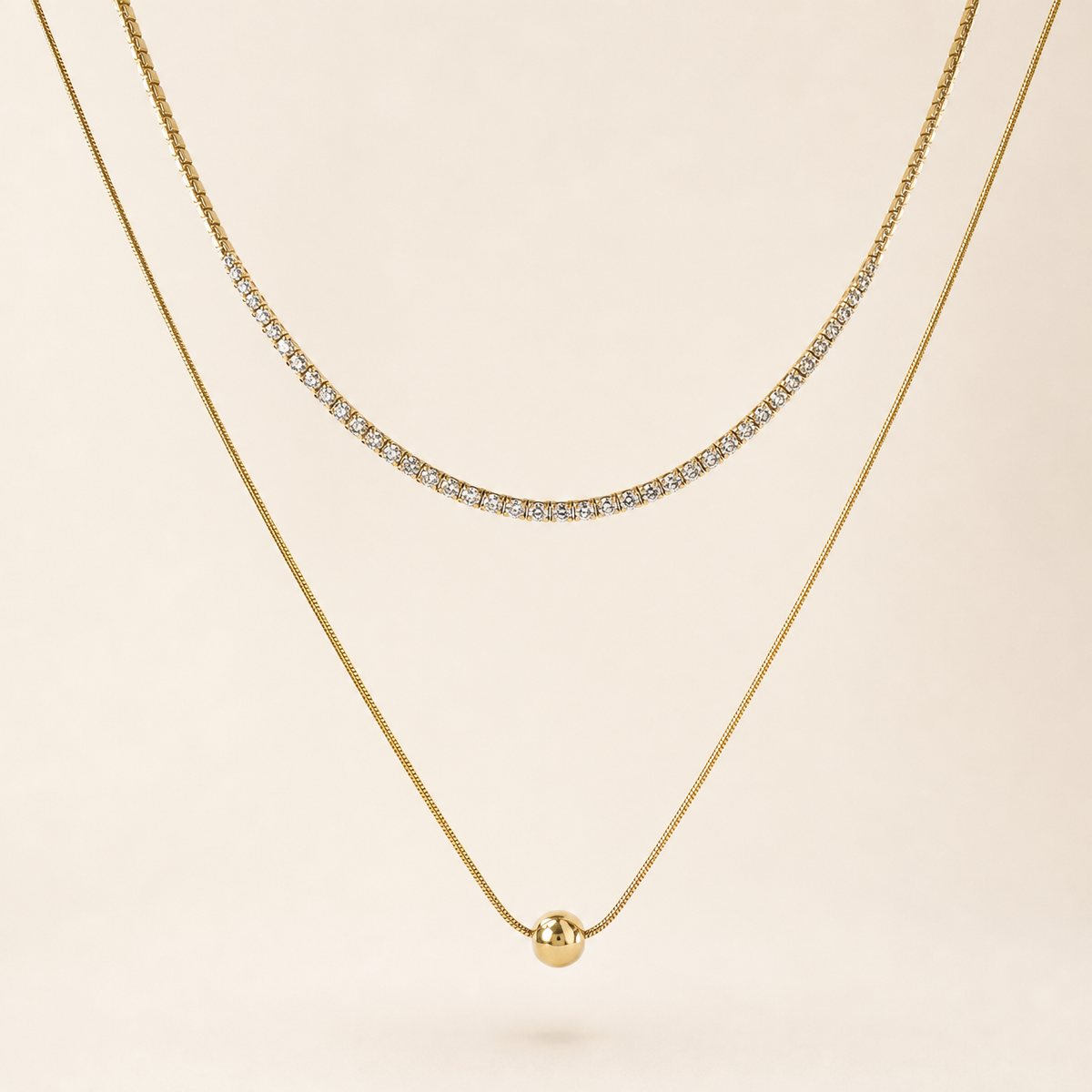 Two separate gold-tone necklaces, polished finish. Necklace one is a single-strand tennis-style chain of small clear round faceted stones, each in an individual gold box/prong mounting linked in a continuous articulated line; stone count is not clearly resolvable at the clasp ends and is withheld, stones are uniform and tightly spaced with no gaps; chain run is roughly 60-70 times one stone width, no extender visible.