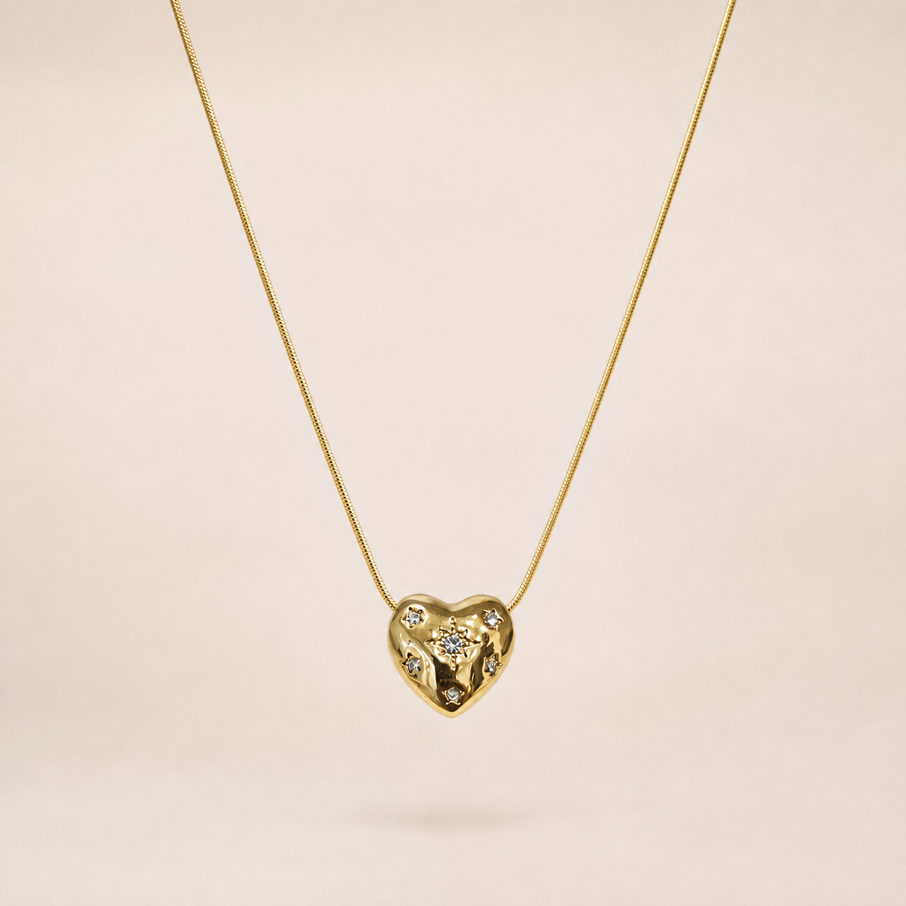 Single pendant necklace. Yellow-gold-tone metal with a polished finish. Construction is one fine round snake chain of small gauge, a single continuous strand with no branches, passing directly through a fixed heart-shaped pendant so the pendant sits centrally on the chain run. The visible chain run is approximately thirty times the width of the heart pendant; no extender chain is visible, and no working clasp is visible in the image, so closure, extender and terminal-tag details cannot be confirmed.