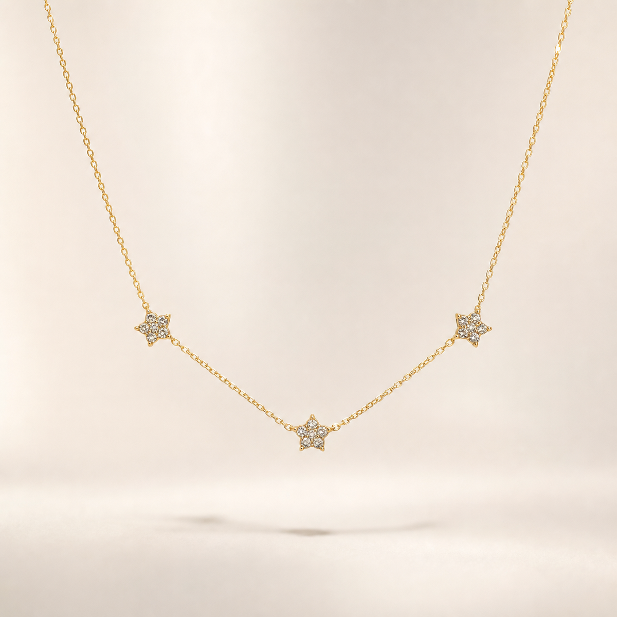 A single necklace of yellow-gold-toned metal with a polished finish, built as one strand of fine, small-gauge cable chain carrying three fixed star-shaped stations set with clear faceted stones. No clasp, extender or terminal tag is visible; the closure end is partly obscured, so only the decorated front run is fully resolvable. The chain run is roughly thirty times the width of the largest star station; no extender length can be reported.