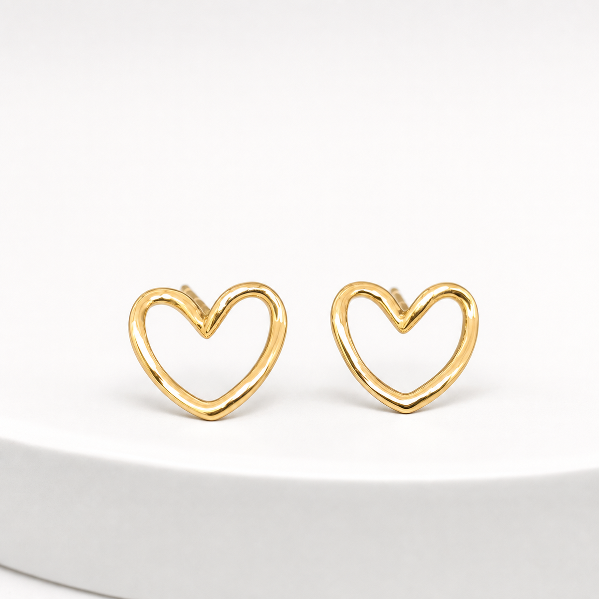 Two ear-worn earrings, a matching-design pair of yellow-gold-tone polished open-heart studs. Each uses a post-and-back stud fitting; short straight posts are partly visible, while the backs are not resolved. Overall drop is minimal, approximately one times the widest heart width. Construction is a single rigid rounded-wire open heart outline with no articulation and no suspended sections.