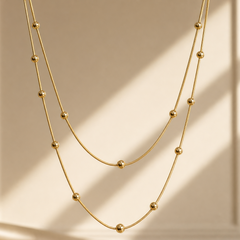 A single three-strand necklace of yellow-gold-tone metal with a bright polished finish. All three strands are fine snake chains of the same small link gauge, joined at a common back section (partly obscured) so the strands run parallel at graduated lengths: the shortest run is roughly 55 times the width of the largest bead component, the middle about 65, and the longest about 75. No extender is visible; the closure is not resolvable in the visible area.